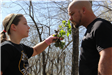 Young girl holds branch with leaves for man to smell